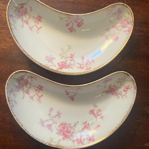 May include: Two vintage, white, crescent-shaped serving dishes with a pink floral pattern and gold trim.