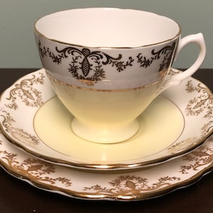 May include: A white teacup and saucer set with a yellow rim and gold floral pattern.