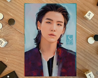 May include: A portrait illustration of a person with long dark hair, wearing a dark red jacket with a white shirt underneath. The background is a light blue with a white crescent moon and the text "APJ" in a circle.