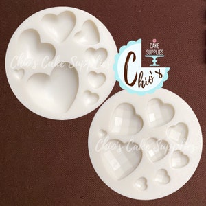 May include: Two white silicone heart-shaped molds. One mold has smooth hearts, the other has textured hearts. The molds are for making cake decorations.