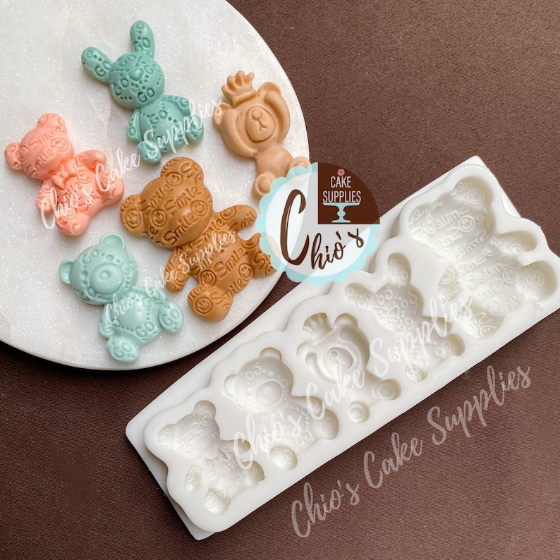 Pu&ograve; includere: Stampo in silicone con sei cavit&agrave; a forma di orso. Lo stampo &egrave; bianco e ha una superficie testurizzata. Lo stampo &egrave; su una superficie marrone. Ci sono cinque piccoli dolci a forma di orso colorati su un piatto bianco accanto allo stampo.