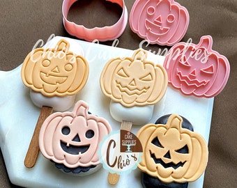 May include: A collection of Halloween-themed cake pops and pumpkin-shaped cookie cutters. The cake pops feature orange, peach, and black frosting with jack-o'-lantern faces. The cookie cutters are pink and shaped like pumpkins. The image includes the text "Chio's Cake Supplies".