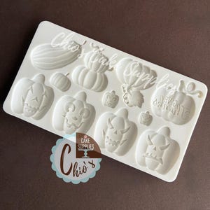May include: A white silicone mold featuring various Halloween-themed pumpkin designs. The mold includes pumpkins with carved faces, a watermelon, and the text "Chio's Cake Supplies".