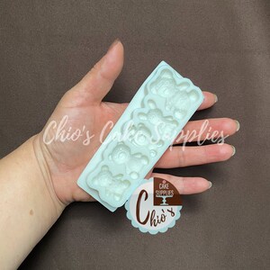 Pu&ograve; includere: Stampo in silicone bianco con quattro forme di orsacchiotti. Lo stampo &egrave; su una mano.