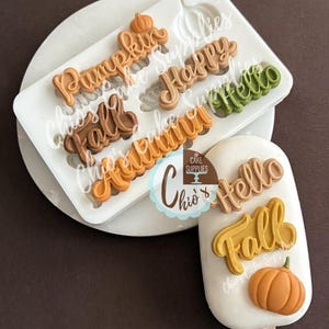 May include: A white silicone mould with the words "Pumpkin", "Happy", "Fall", "Autumn", and "Hello" in autumnal colours. A white ice lolly with the words "Hello", "Fall", and a pumpkin.