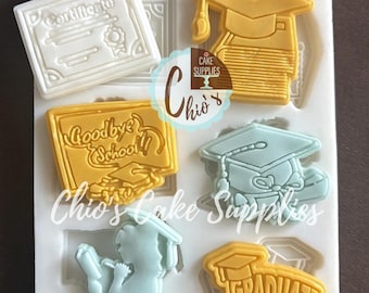 May include: A white silicone mold with graduation-themed designs. The mold includes shapes of a graduation cap, diploma, and the words "Goodbye School" and "Graduate". The mold is for cake decorating and has the text "Chio's Cake Supplies".