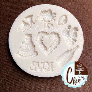 May include: White silicone mold with various wedding-themed designs, including a cake, a heart wreath, a bouquet, a bottle of champagne, two rings, and the word "LOVE".