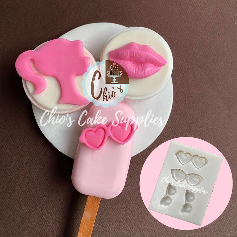 May include: Pink cake decorations including a silhouette, lips, and popsicle with heart-shaped sunglasses. The image also shows a silicone mold with heart and cat-eye shaped glasses. The text "Chio's Cake Supplies" is visible.