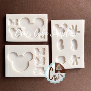 May include: Four white silicone molds for baking. The molds feature various Mickey Mouse themed designs, including Mickey Mouse heads, bows, and a nurse's hat. The text "Chio's Cake Supplies" is visible on the molds.