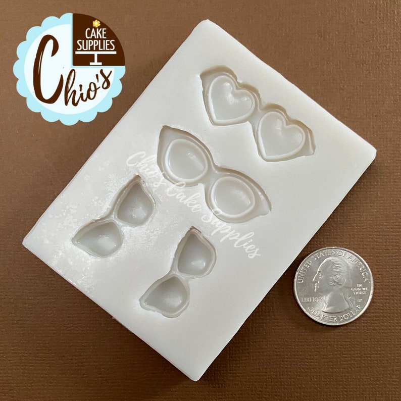 May include: A white silicone mold featuring four pairs of sunglasses in different styles, including heart-shaped and cat-eye designs. The mold is labeled "Chio's Cake Supplies". A US quarter is next to the mold for size reference.