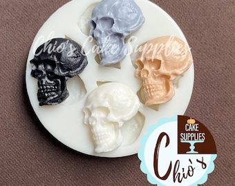 May include: A white silicone mould featuring five skull shapes in black, grey, peach, and white. The mould is round with the text "Chio's Cake Supplies" in the image.