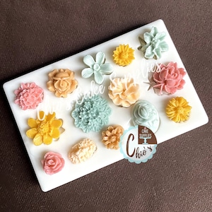 May include: A white silicone mould with 12 different flower designs. The mould is filled with colourful fondant flowers in shades of pink, yellow, green, and peach.