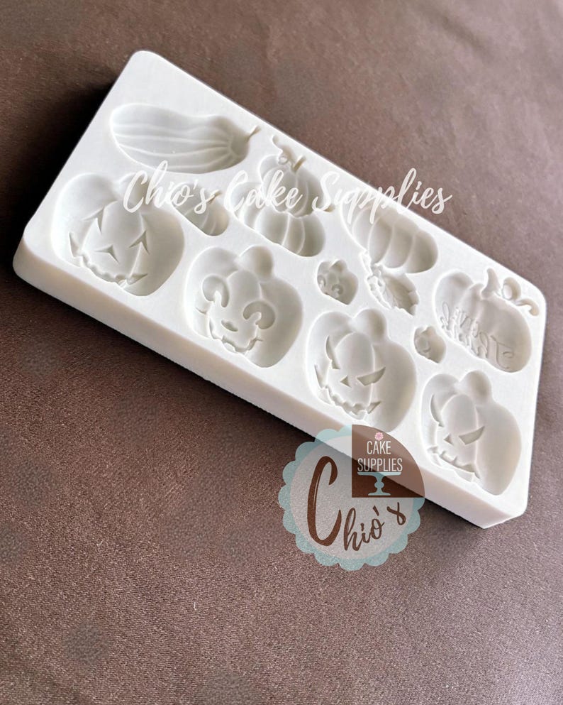 May include: A white silicone mold featuring various Halloween-themed shapes, including pumpkins and gourds. The mold has multiple cavities for creating decorative elements. The text "Chio's Cake Supplies" is visible on the mold.