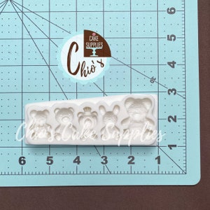 Pu&ograve; includere: Stampo in silicone bianco con cinque cavit&agrave; per realizzare dolcetti a forma di orsacchiotto. Lo stampo &egrave; su un tappetino a griglia blu con segni in pollici.