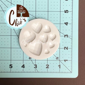 May include: A white silicone mold with eight heart-shaped cavities. The mold is designed for making chocolate or candy hearts.