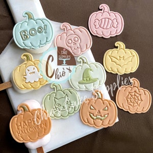 以下が含まれることがあります： ハロウィーンをテーマにした、さまざまなパステルカラーのカボチャ型のデコレーションのコレクション。 スカル、猫、魔女の帽子、「BOO！」と「HAPPY HALLOWEEN」の文字などのデザインが施されています。