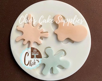 May include: Silicone mold with three shapes: a pink splatter, a peach splatter, and a light blue splatter. The mold is white and has the text "Chio's Cake Supplies" on it.