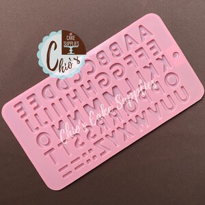 May include: Pink silicone mold with raised letters of the alphabet, A through Z, and two rows of equal signs. The mold is for making fondant or chocolate letters for cake decorating.