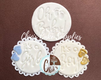 May include: White fondant cake toppers with embossed text and baby foot designs. One topper says "Oh Baby!" and two others say "It's a Girl" and "It's a Boy". The "Girl" topper has blue feet, and the "Boy" topper has gold feet. The brand name "Chio's Cake Supplies" is also visible.
