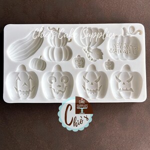 May include: A white silicone mold for making Halloween-themed decorations. The mold features various pumpkin designs, including jack-o'-lantern faces and a pumpkin with the word "GIVE" on it. The mold is labeled "Chio's Cake Supplies".