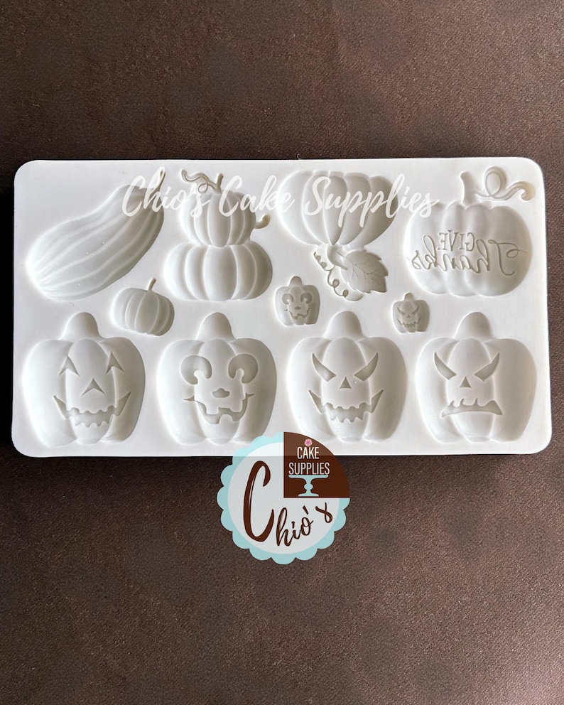 May include: A white silicone mold for making Halloween-themed decorations. The mold features various pumpkin designs, including jack-o'-lantern faces and a pumpkin with the word "GIVE" on it. The mold is labeled "Chio's Cake Supplies".