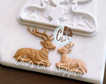 Könnte beinhalten: Eine weiße Silikonform und zwei braune Hirsch-Kuchendekorationen auf einer weißen Oberfläche. Die Form hat die Form von zwei Hirschen. Die Dekorationen sind detailliert und haben ein Geweih. Das Bild enthält den Text "Chio's Cake Supplies".