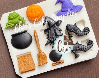 May include: A white silicone mold filled with Halloween-themed shapes. Includes a jack-o'-lantern, witch hat, cauldron, witch, broom, frog, spell book, and witch shoes. The text "Chio's Cake Supplies" is visible.