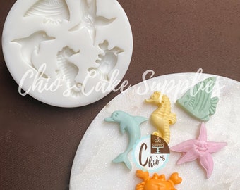 May include: Silicone mold with six different sea creature designs: a starfish, a seashell, a seahorse, a crab, a dolphin, and a fish. The mold is white and the sea creatures are in various colors.