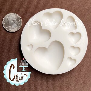 May include: White silicone mold with seven heart-shaped cavities. The mold is round and has a diameter of approximately 3 inches. The hearts range in size from small to large.