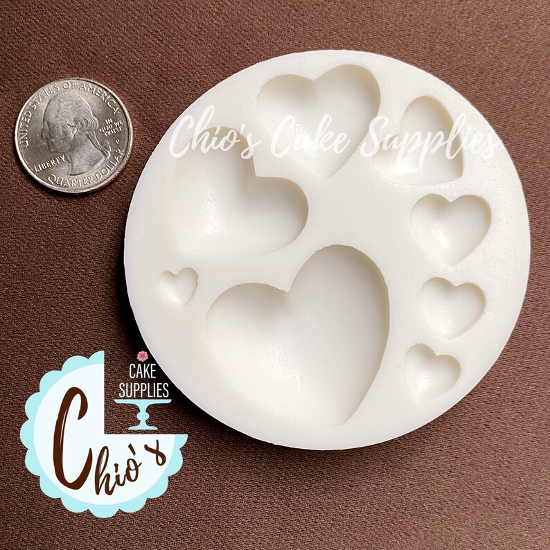 May include: White silicone mold with seven heart-shaped cavities. The mold is round and has a diameter of approximately 3 inches. The hearts range in size from small to large.