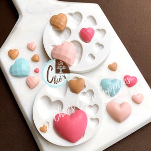 May include: A silicone mold for making heart-shaped fondant decorations. The mold has multiple heart-shaped cavities of different sizes. There are also several finished fondant hearts in various colors, including pink, blue, and brown.