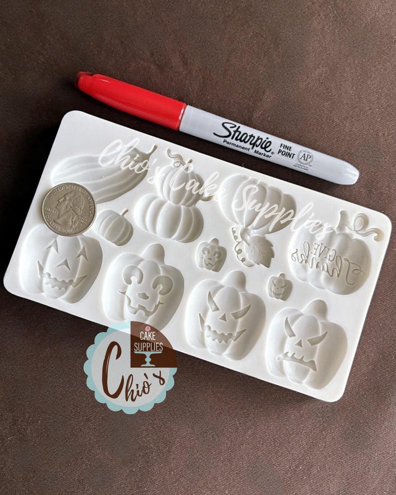 May include: A white silicone mold featuring various pumpkin designs, including jack-o'-lantern faces and pumpkin shapes. A red and silver Sharpie marker and a US quarter are next to the mold. The mold is from Chio's Cake Supplies.