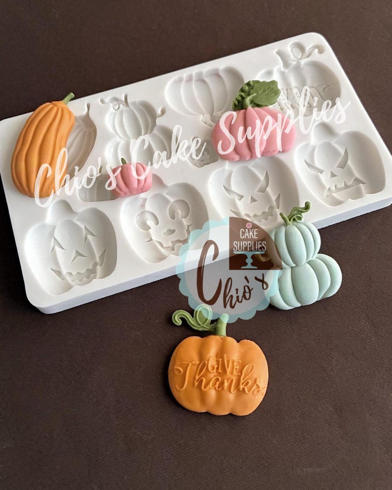 May include: A white silicone mold with pumpkin shapes and several finished fondant pumpkins in orange, pink, and blue. One orange pumpkin has the words "Give Thanks" on it. The text "Chio's Cake Supplies" is also visible.