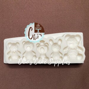 Pu&ograve; includere: Stampo in silicone con cinque cavit&agrave; a forma di orsacchiotti. Lo stampo &egrave; bianco e ha una superficie testurizzata. Lo stampo &egrave; etichettato "Chio's Cake Supplies".