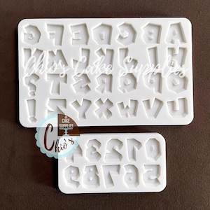 Puede incluir: Dos moldes de silicona blancos para hornear. El molde superior tiene las letras A a la Z en una fuente irregular y dentada. El molde inferior tiene los números del 0 al 9 en la misma fuente.