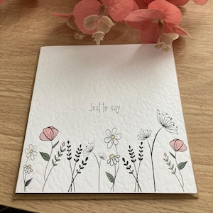 May include: A white card with the text "Just to say..." and a black and white illustration of a field of flowers. The flowers are pink, white, and green.