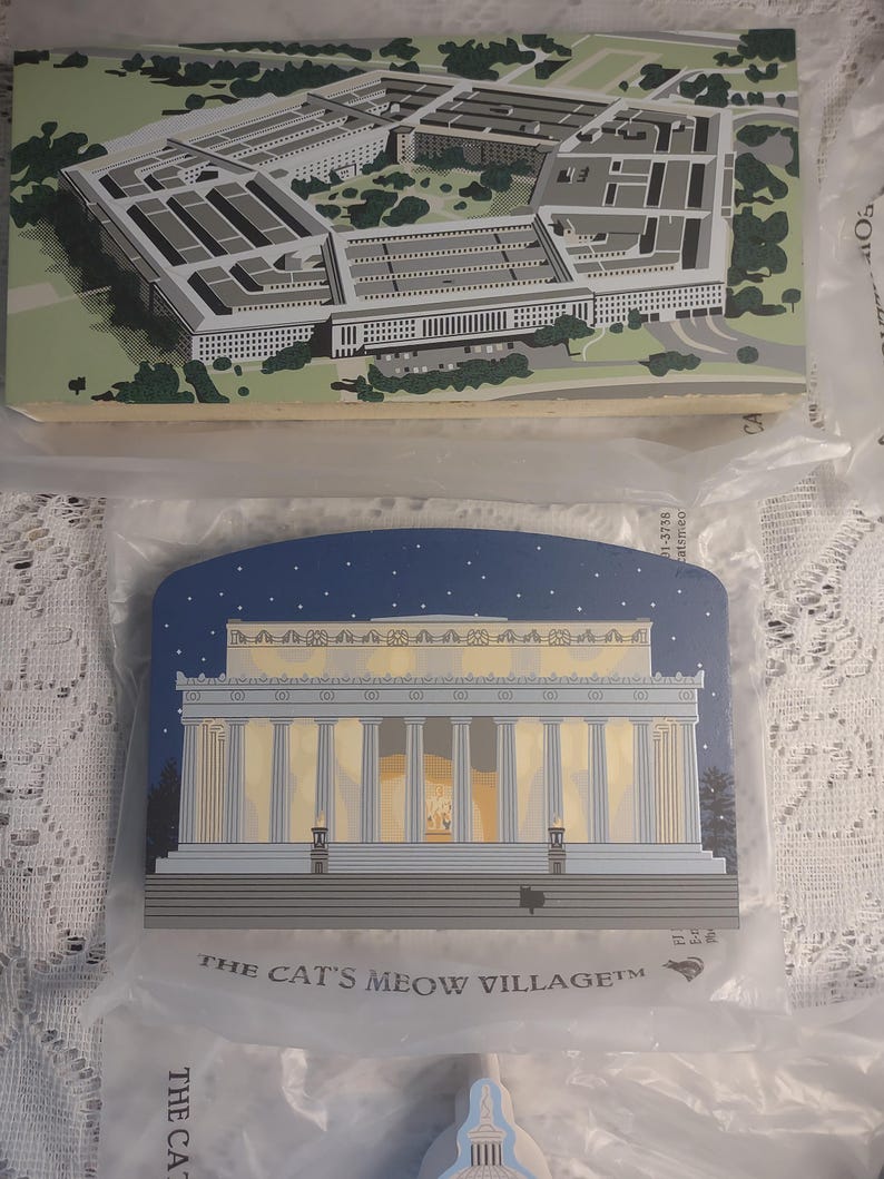 May include: Two wooden plaques featuring architectural illustrations. The top plaque depicts the Pentagon in shades of gray and green. The bottom plaque shows the Lincoln Memorial under a starry night sky. The text "THE CAT'S MEOW VILLAGE" is printed on the bottom plaque.