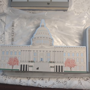 May include: A set of Capitol Building-shaped decorative items. The main item is a detailed illustration of the U.S. Capitol Building, featuring a white facade, a large dome, and a blue sky background. The text "THE CAT'S MEO" is visible.