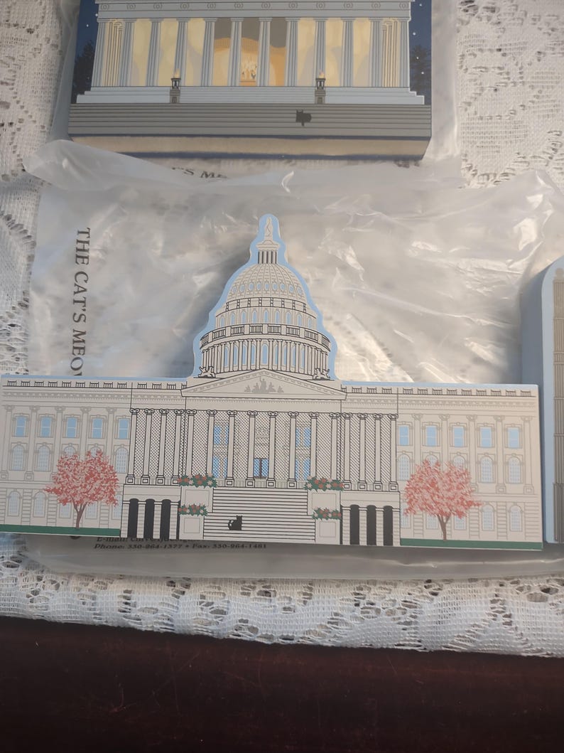 May include: A set of Capitol Building-shaped decorative items. The main item is a detailed illustration of the U.S. Capitol Building, featuring a white facade, a large dome, and a blue sky background. The text "THE CAT'S MEO" is visible.