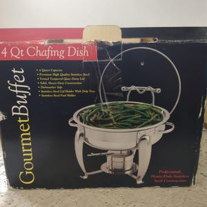 May include: A stainless steel 4-quart chafing dish with a glass lid, filled with green beans. The box reads "Gourmet Buffet" and lists features like heavy-duty construction and dishwasher-safe. The text also says "Professional, Heavy-Duty Stainless Steel Construction."