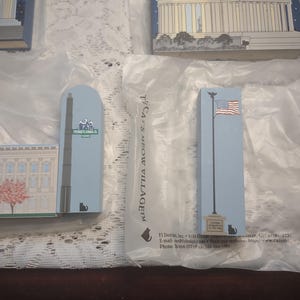 May include: A collection of rectangular wooden ornaments featuring iconic American landmarks. The ornaments are painted in various colors and designs, including the U.S. Capitol building, a tall obelisk, and a flagpole with the American flag. The text "PENNSYLVANIA 1600" is visible.
