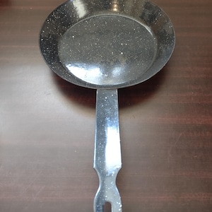 Peut inclure: Une poêle en fonte émaillée noire avec une finition mouchetée et une longue poignée noire.