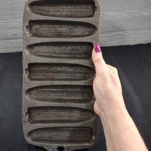 May include: A cast iron cornbread pan with six individual molds. The pan is dark gray and has a textured surface.
