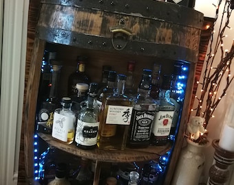 May include: A wooden barrel bar cart with shelves for storing bottles of spirits. The shelves are lit with blue LED lights. The cart is decorated with autumn-themed knitted pumpkins.