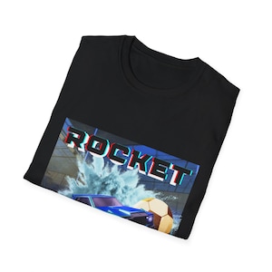 Może przedstawiać: Czarny t-shirt z grafiką z napisem "ROCKET" w efekcie 3D. Grafika zawiera niebieski samochód, piłkę nożną i rozprysk wody, sugerując motyw sportowy lub gamingowy.