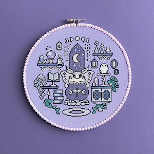 Könnte beinhalten: Ein Kreuzstich-Stickrahmen mit einer magischen Szene. Das Design zeigt einen Kessel, eine Eule, Bücher und eine Kristallkugel in Lila, Blau und Weiß. Der Rahmen ist mit kleinen, weißen Perlen umrandet. Ein dekoratives Element für die Wand.