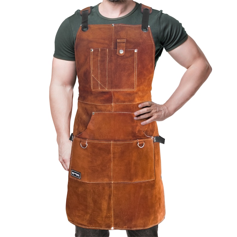 May include: A brown leather apron with multiple pockets and adjustable straps. The apron has a rugged, workwear aesthetic, with visible stitching and metal hardware. It is designed to protect clothing during various tasks.