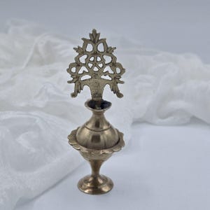 May include: A silver metal perfume bottle with an ornate, filigree design on the top. The bottle has a round body and a small, round base.