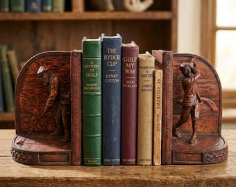Könnte beinhalten: Braune Buchstützen aus Holz mit Golf-Motiv. Die Buchstützen zeigen geschnitzte Golferfiguren. Zwischen den Buchstützen befinden sich Bücher mit Titeln wie "A History of Golf" und "The Ryder Cup". Die Bücher sind in verschiedenen Farben.