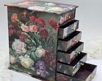 May include: A wooden jewelry box with five drawers, featuring a floral print of roses and carnations in shades of pink, red, and white. The box has gold-toned drawer pulls.